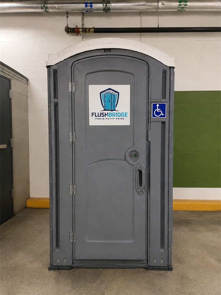 Gray ADA accessible portable restroom standing indoors beside a green wall and yellow floor line