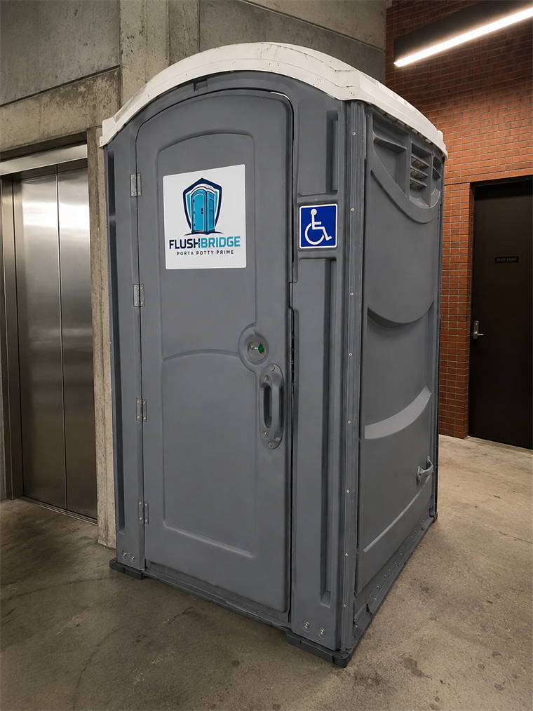 Gray ADA accessible portable restroom standing beside an elevator in a concrete building lobby