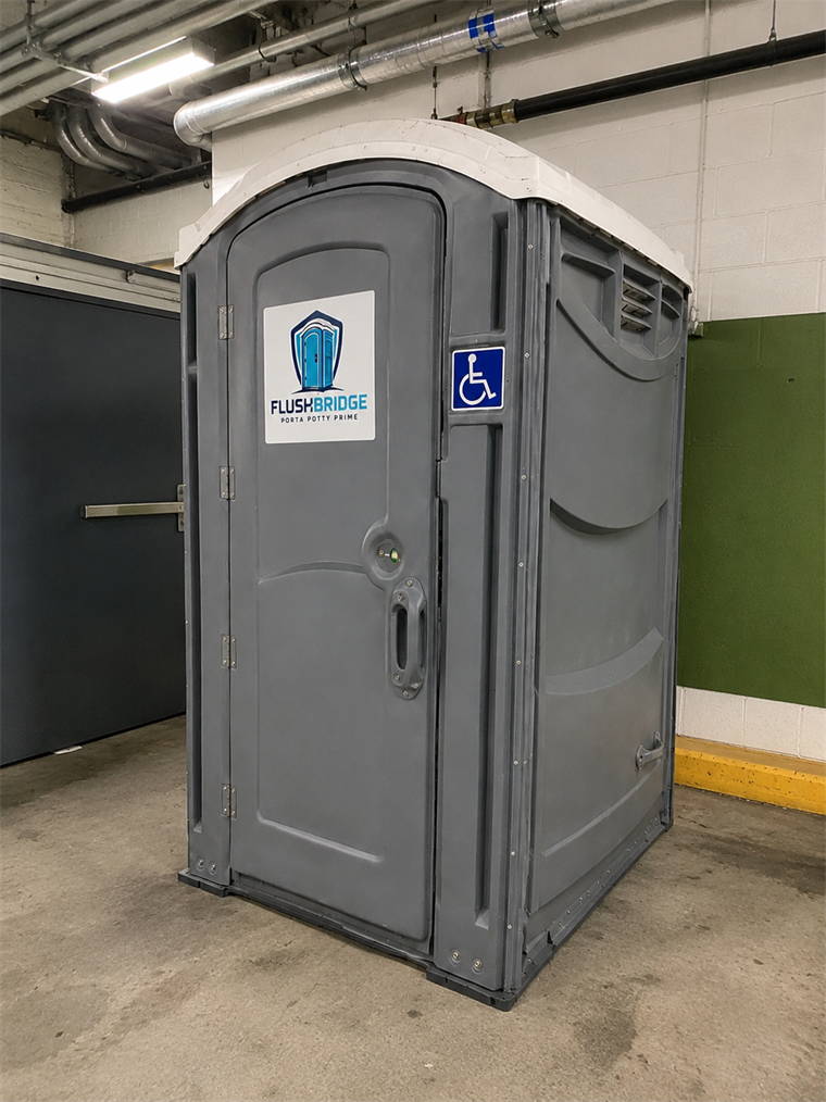 Gray ADA accessible portable restroom standing on a concrete floor beneath exposed service pipes