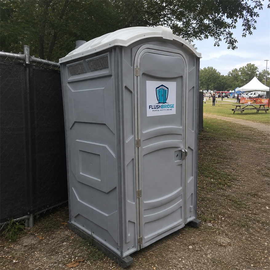 Gray portable toilet standing beside a fence line