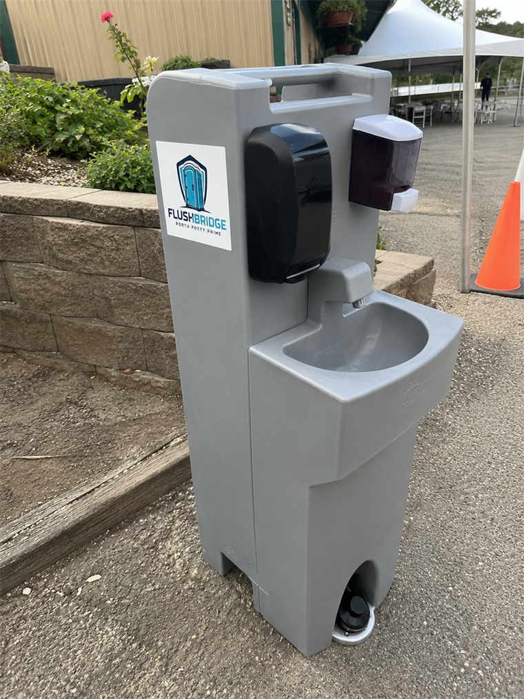 Gray portable handwashing station with two basins and soap dispensers standing outdoors