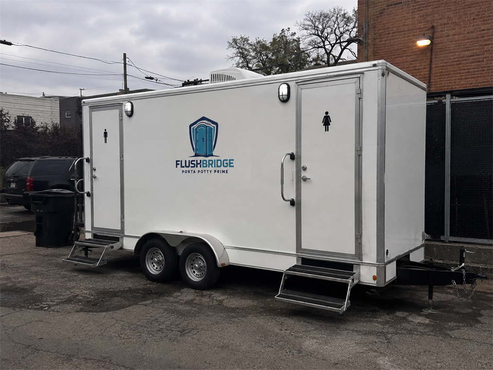 White restroom trailer parked on asphalt beside a building, entrance doors facing the lot
